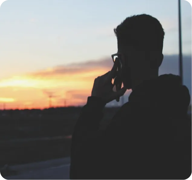 Silhouette of person talking on phone against sunset sky.