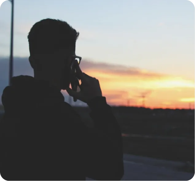Person silhouetted against sunset, holding phone to ear, standing outdoors.