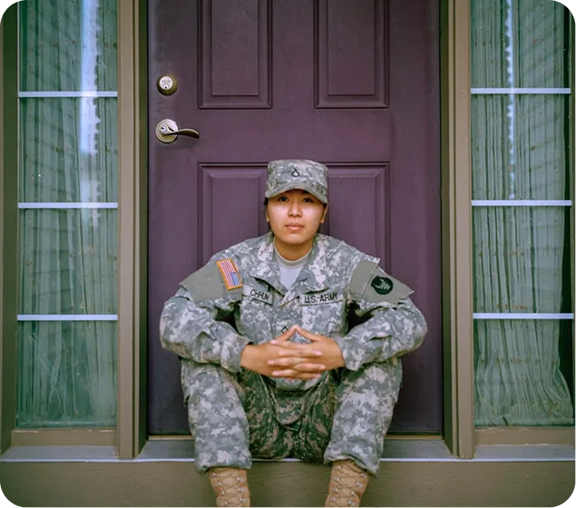 A soldier in camouflage uniform sits on a porch in front of a purple door.