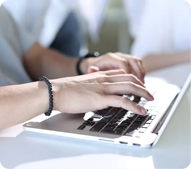 Person typing on a silver laptop with a bracelet on their wrist.