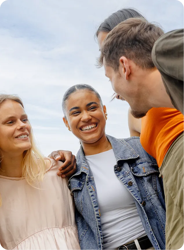 Four friends smile and laugh together outdoors, enjoying a sunny day.