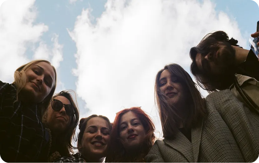 Six people pose together outdoors, looking up at a bright sky with clouds.