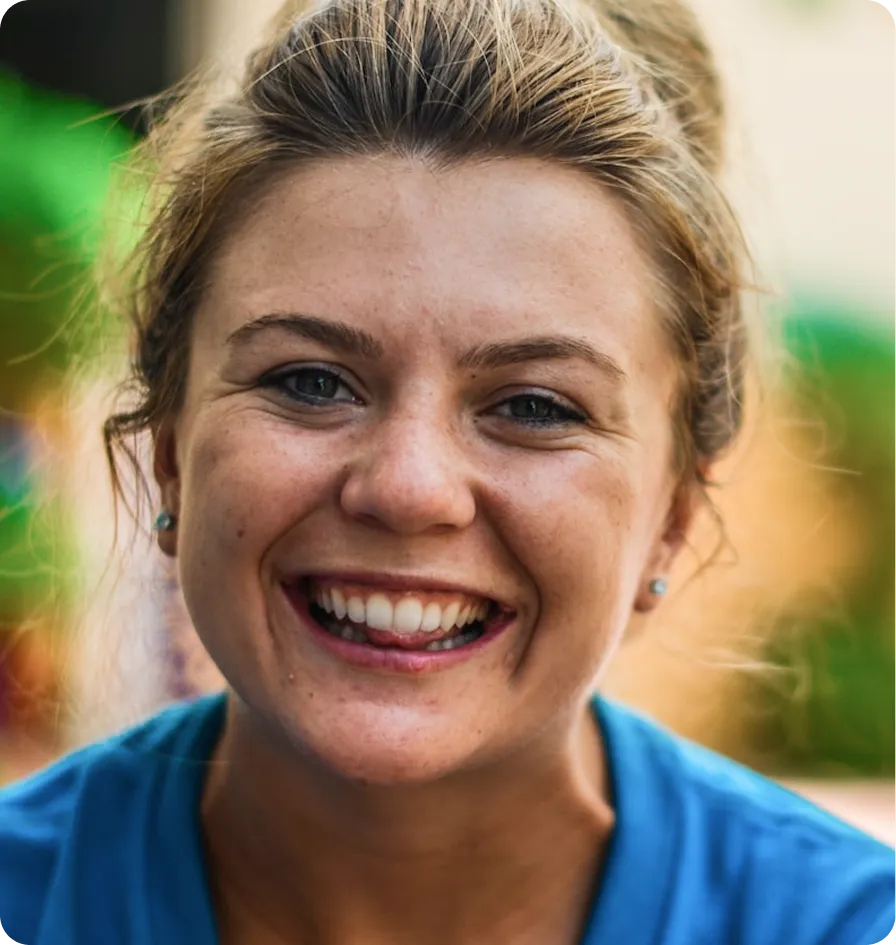 A smiling woman with blonde hair in a bun, wearing a blue shirt, against a blurred background.