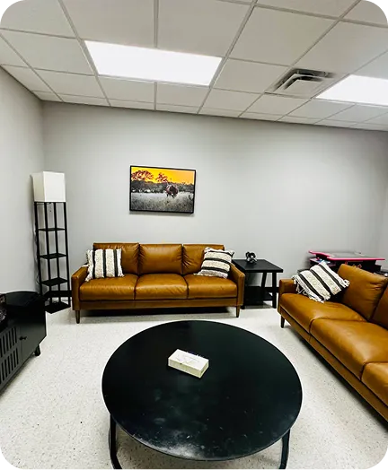 A modern living room with two brown leather sofas, a black coffee table, and a framed painting on the wall.