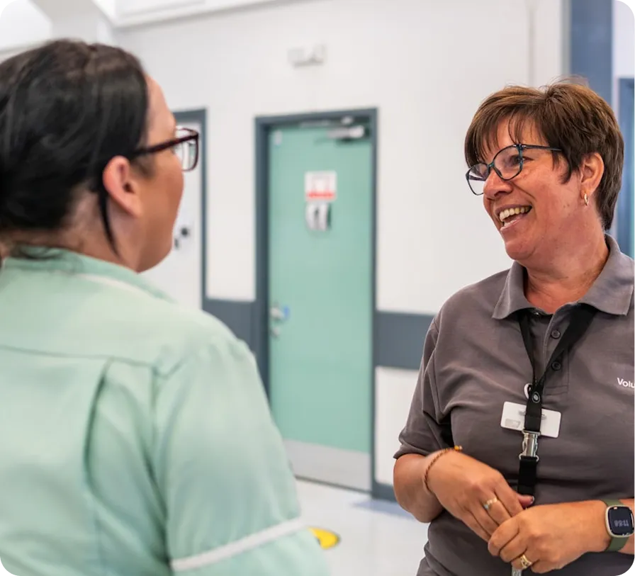 Two women in a hallway, one in scrubs, the other in a uniform, smiling and talking.
