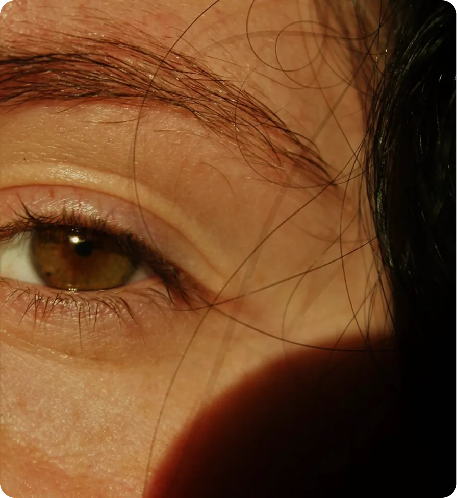 Close-up of a person's eye with brown iris and eyebrow, hair partially covering face.