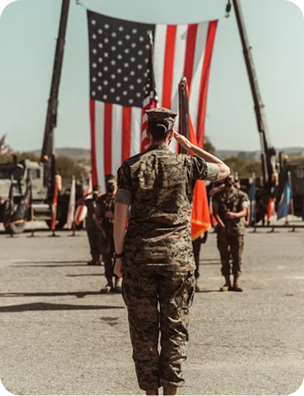A soldier salutes in front of a large American flag at a military ceremony.