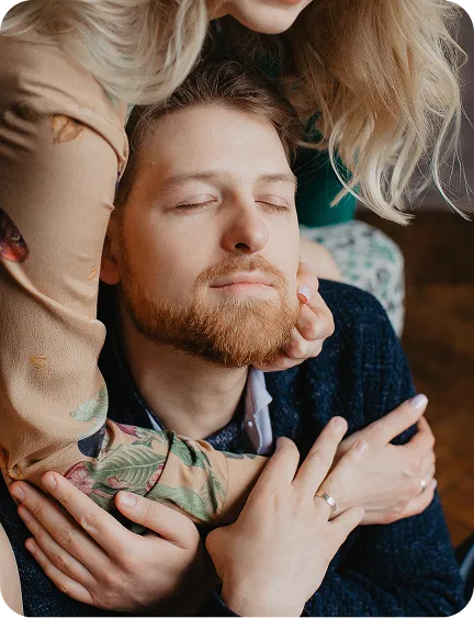 A man and woman embrace, the woman's arm around his neck, both with eyes closed, suggesting affection and intimacy.